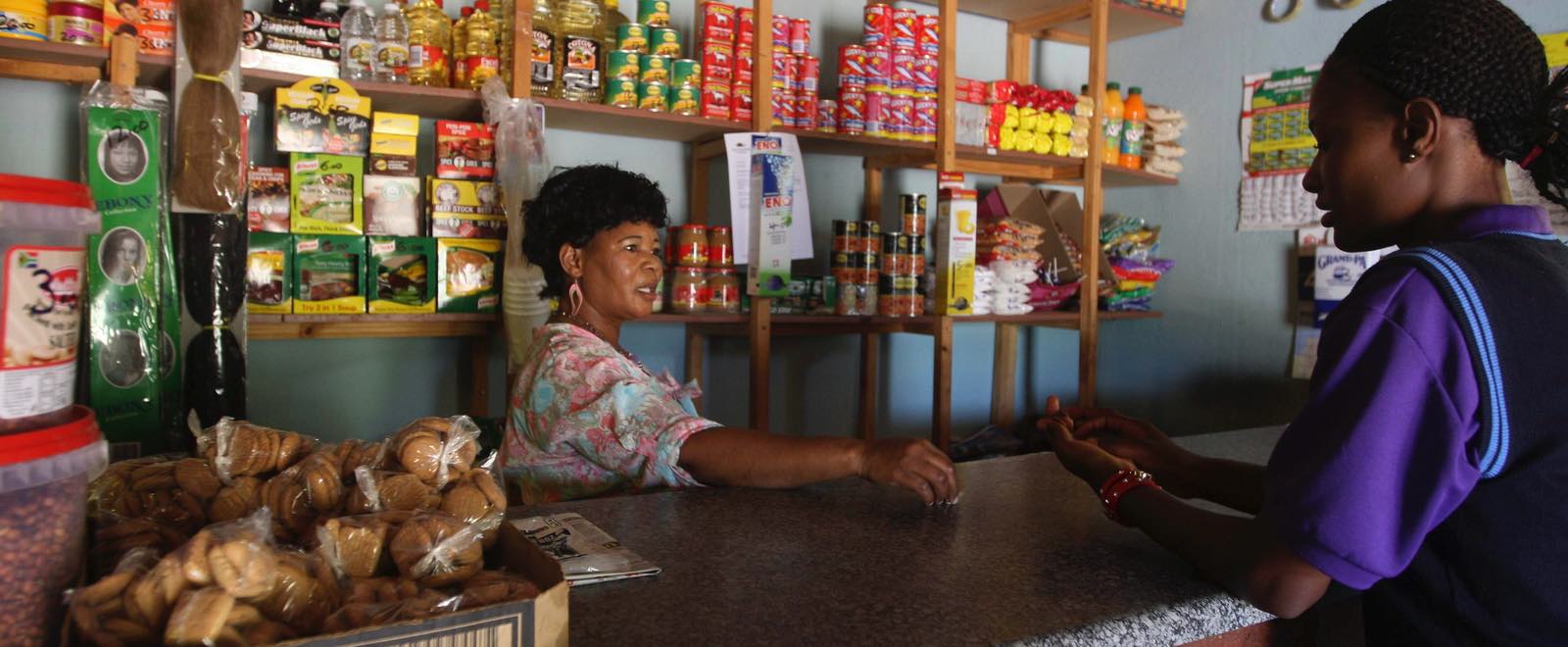 A spaza shop owner sells to a customer